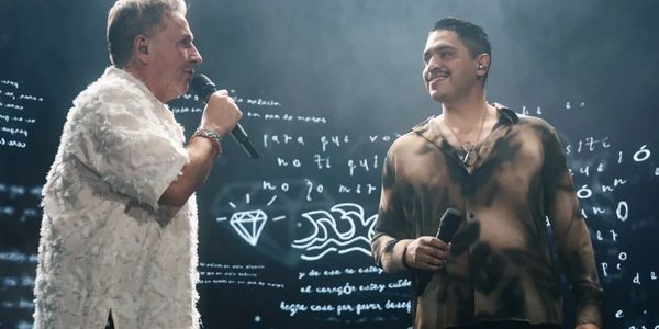 Two men singing on stage with artistic background visuals.
