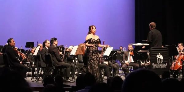 A female opera singer performs with an orchestra on stage.
