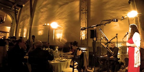 A woman in a red dress sings to diners in a warmly lit restaurant.