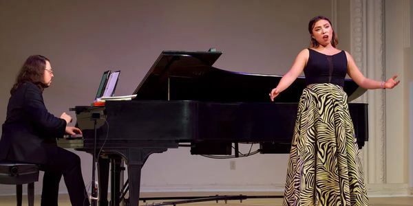 A pianist accompanies a female singer performing on stage.