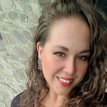 Smiling woman with curly hair posing by a stone wall.