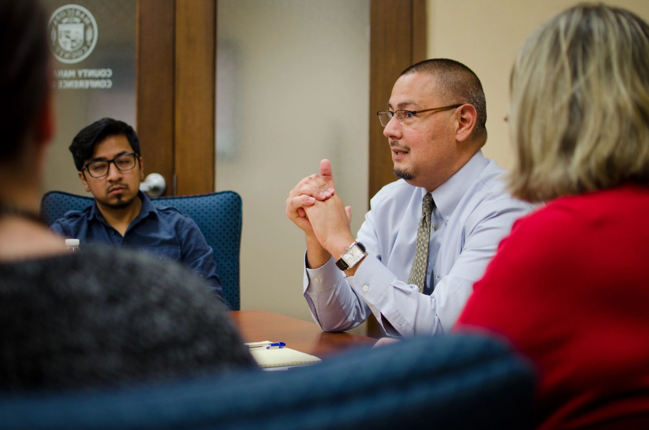 A man speaks during a meeting with attentive participants.