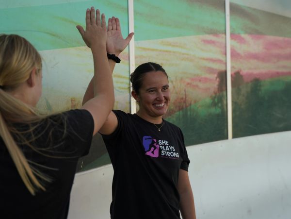 Two women giving a high-five, one wearing a She Plays Strong shirt.