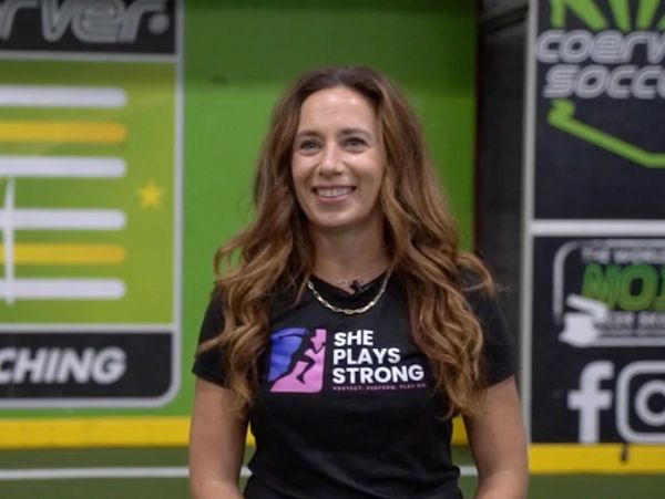 Woman in a "She Plays Strong" t-shirt smiling indoors.