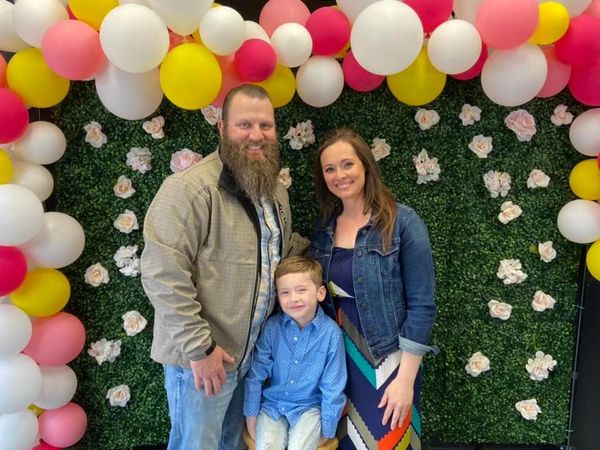 A family of three posing with colorful balloons and flower wall.