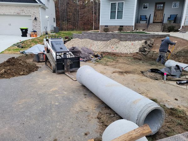 Construction work on a residential driveway with large concrete pipes.