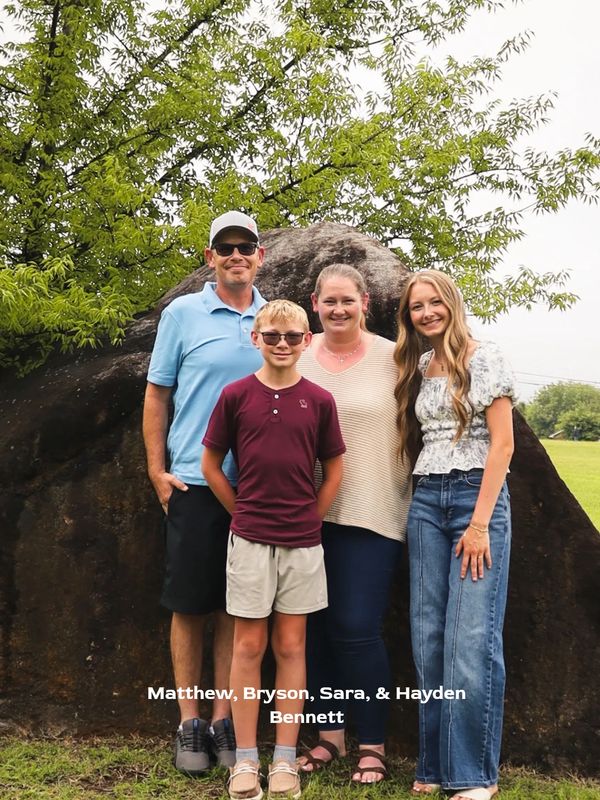 Family of four posing outdoors by a large rock.