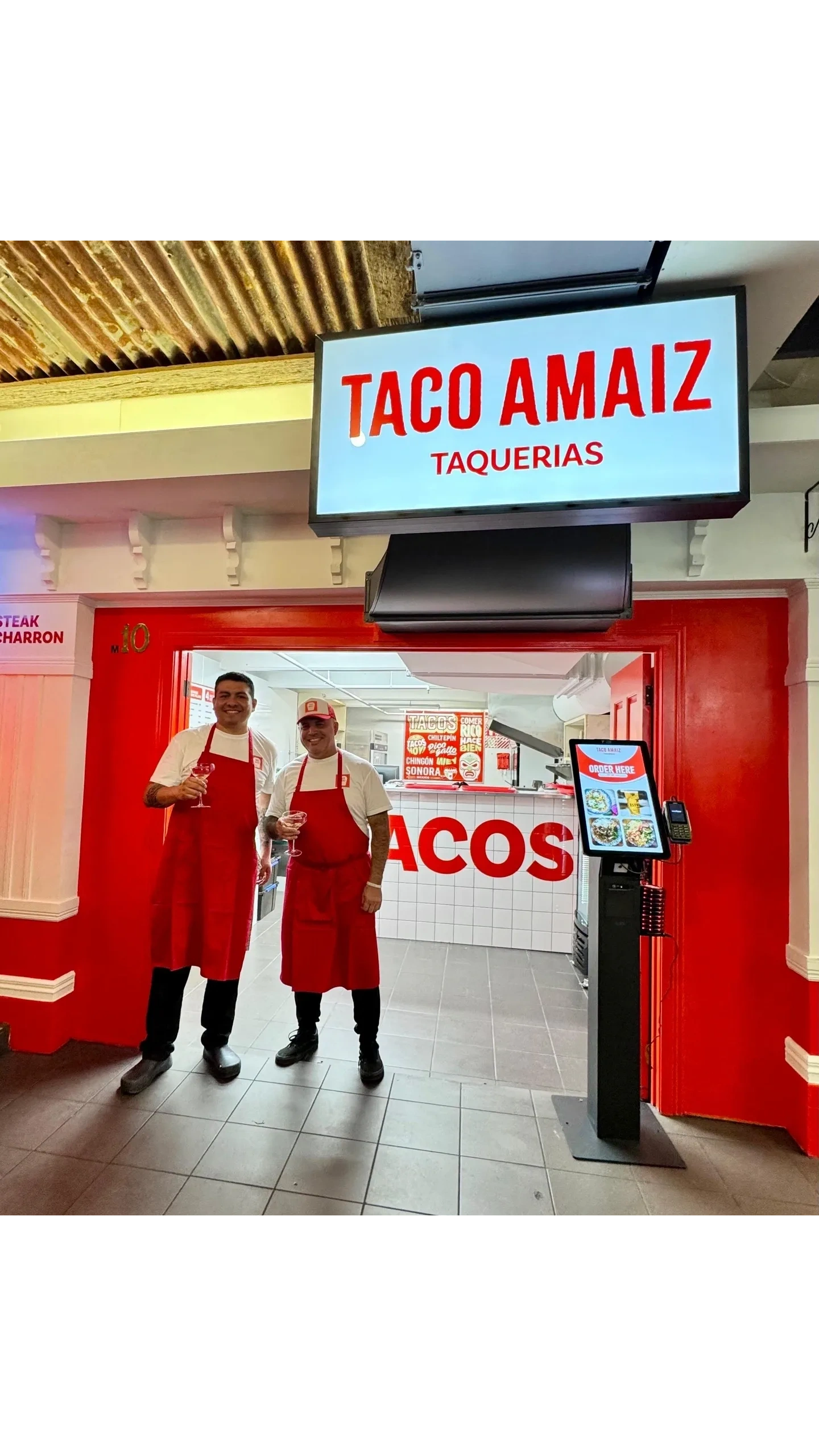 Chef Alfredo Romero and Jose Sanatnader stand outside Taco Amaiz taqueria holding drinks.