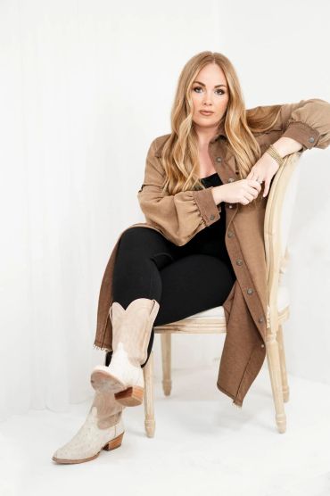 Confident woman in beige coat and boots sitting on a chair.