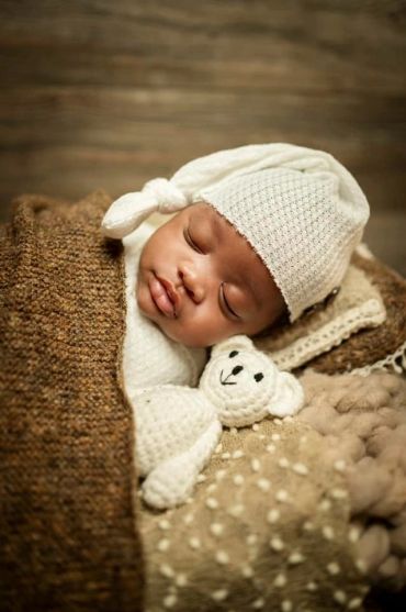 Sleeping baby wrapped in cozy blankets with a knitted hat and teddy bear.