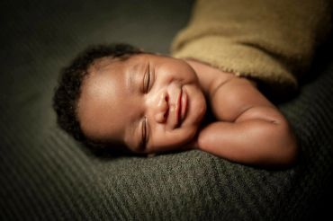 Smiling newborn baby resting peacefully on a soft blanket.