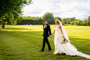 Newlywed couple walking hand in hand on a sunny day in a green park.