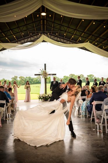 Newlyweds share a romantic dip kiss at their outdoor wedding ceremony.