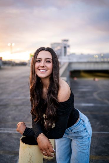Young woman with long hair smiling outdoors during sunset.