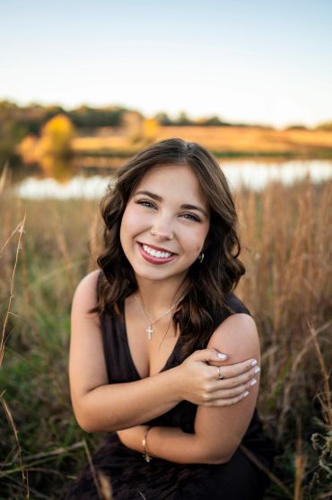 Young woman smiling in a field near a lake during golden hour.