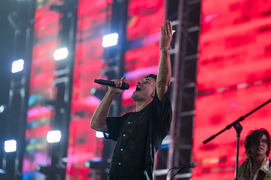 A singer passionately performing on stage with vibrant red background lights.