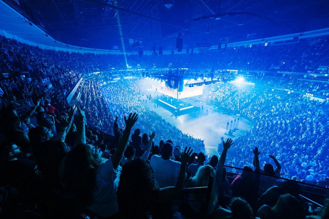 A massive crowd enjoying a concert with blue lighting in a large arena.