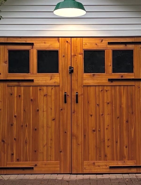 Rustic wooden double doors with black handles and small windows under a green hanging light.