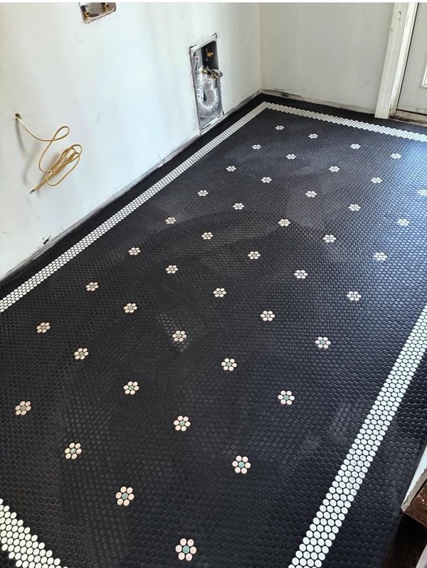 Black tiled floor with white floral patterns and border in a room under renovation.
