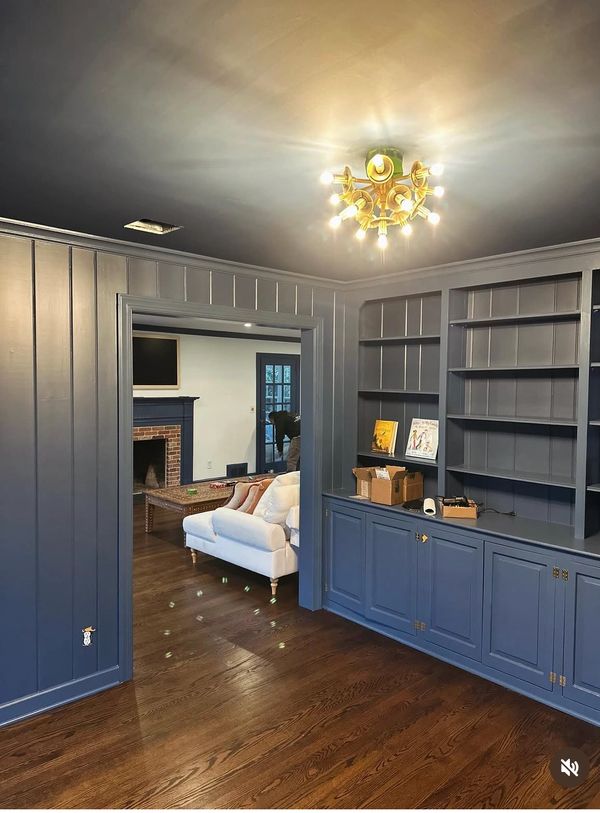 Cozy blue-paneled room with built-in shelves and a warm chandelier.