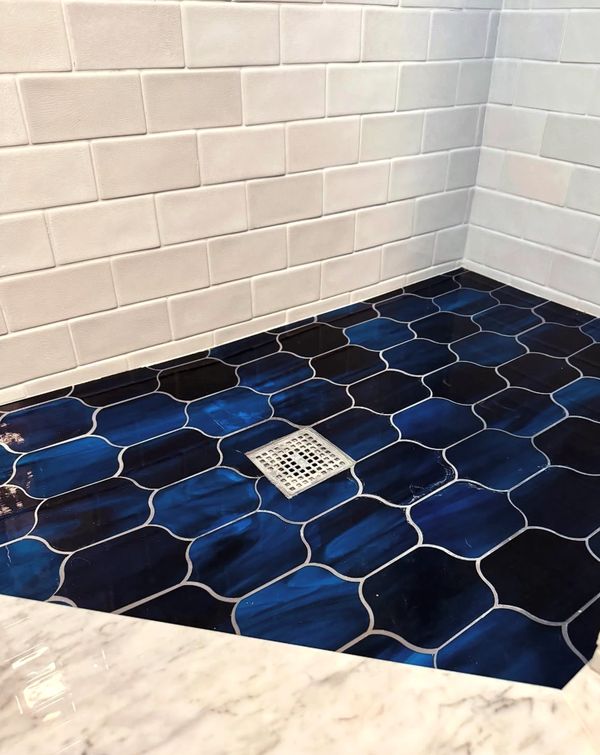 Shower floor with glossy dark blue tiles and white subway tiled walls.