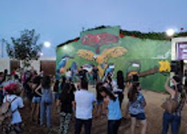 People gathered outdoors near a colorful mural at dusk.