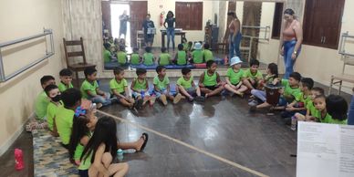 Children sitting in a circle on the floor in a classroom with adults standing nearby.