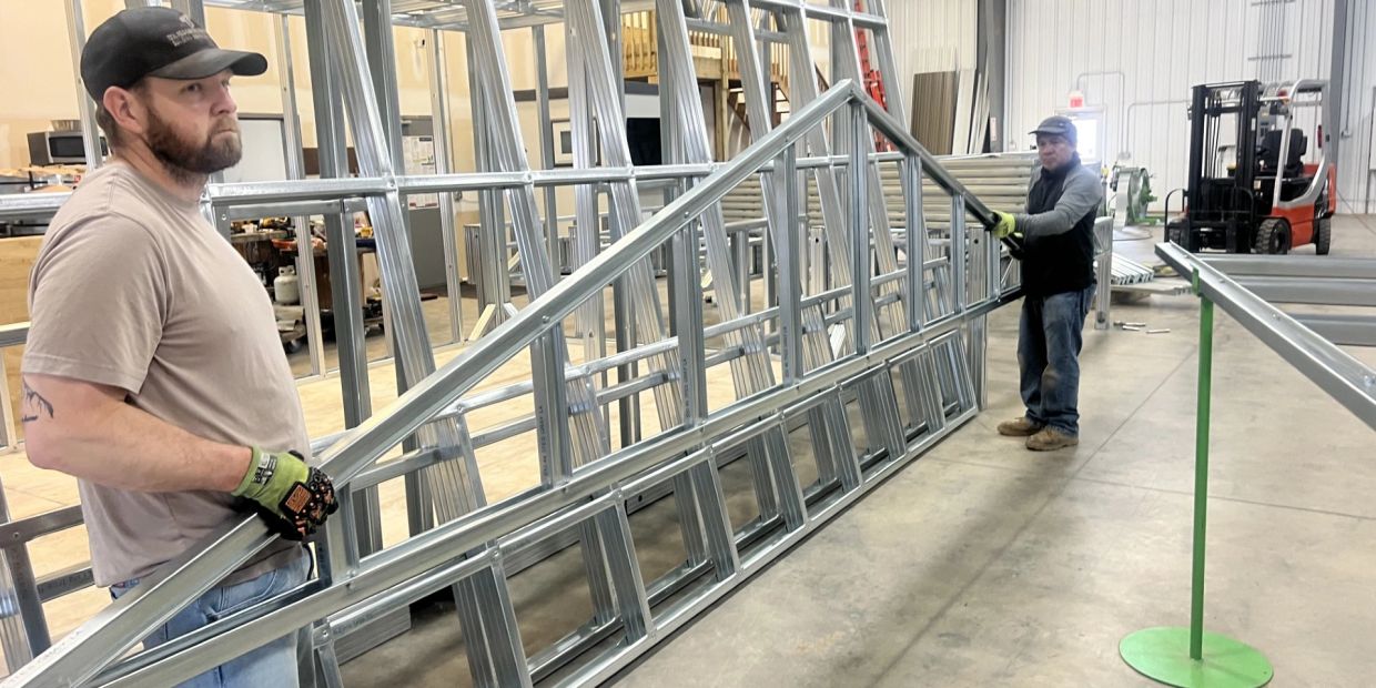 Two workers carry large metal frame indoors.