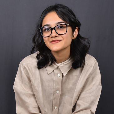 Young woman with glasses smiling against a dark background.