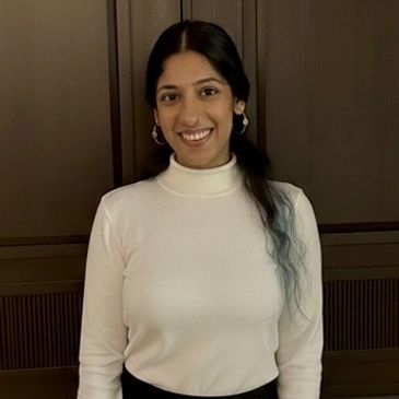 Smiling woman with long dark hair, wearing a white turtleneck and hoop earrings.