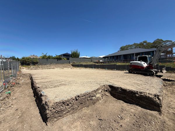 Cleared construction site with excavator under blue sky.