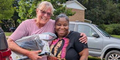 Two women happily posing outdoors with gifts in hand.