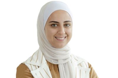 Smiling woman wearing a white hijab and beige outfit.