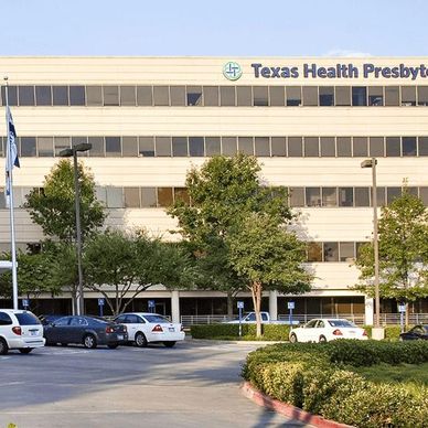 Exterior view of Texas Health Presbyterian hospital with parking lot and cars.