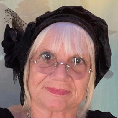 Elderly woman with glasses and a black hat.
