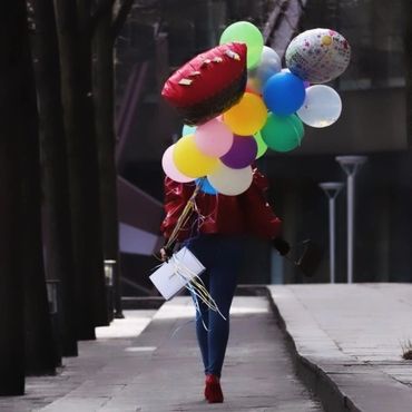 Person walking with colorful balloons and a shopping bag on a city sidewalk.