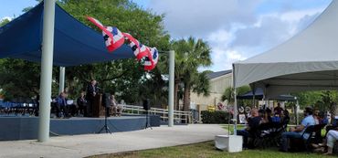 Outdoor event with speakers and audience under tents.