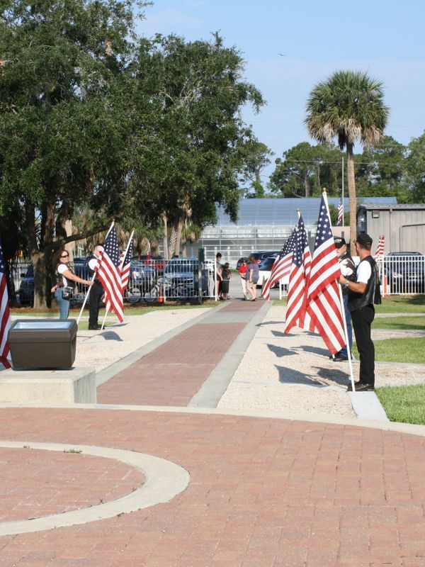 People holding American flags in a park with trees and buildings.