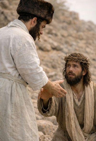 Two men in ancient robes, one wearing a crown of thorns, reaching hands in a rocky setting.