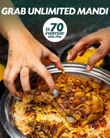 Two hands reaching for a plate of mandi rice with meat and fried onions.