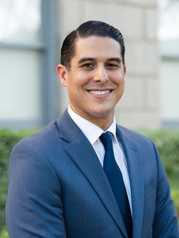 Confident man in a blue suit smiling outdoors.