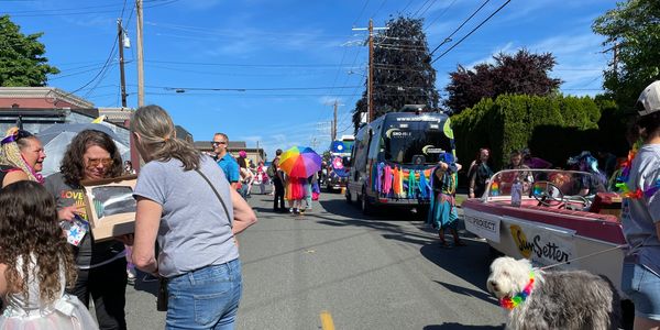 People enjoying a sunny parade with colorful decorations and a dog wearing a rainbow collar.