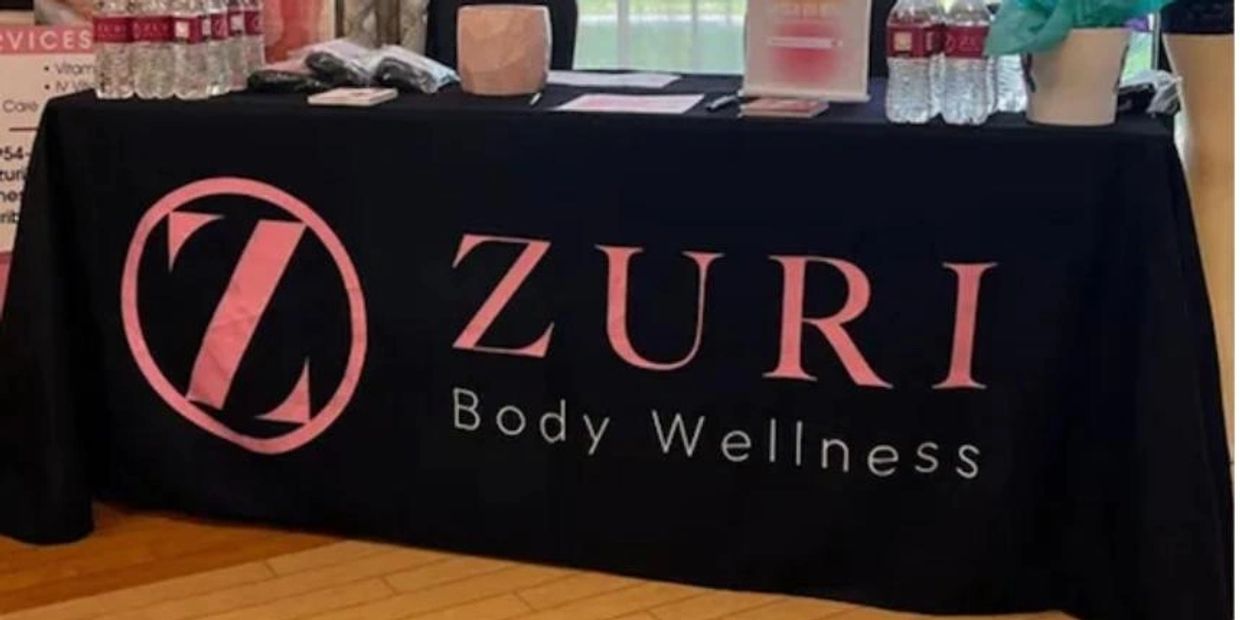 A table with a black cloth displaying the Zuri Body Wellness logo in pink.