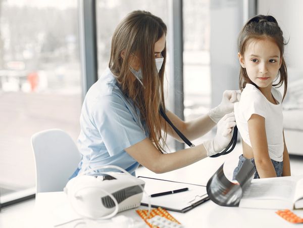 Doctor using a stethoscope to examine a young girl in a medical office.