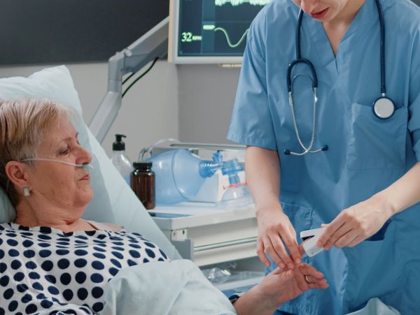 Nurse checks oxygen levels of elderly patient in hospital bed.