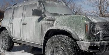 SUV covered in soap foam during a car wash on a sunny day.
