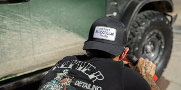 Man wearing a 'Support Blue Collar' cap detailing a vehicle.
