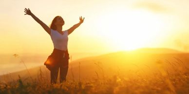 Femme heureuse levant les bras au coucher du soleil.