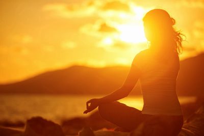 Person meditating by the water at sunset with a serene golden glow.