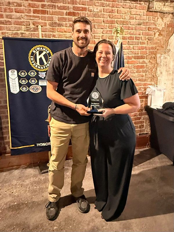 Two people smiling and holding an award at a Kiwanis International event.